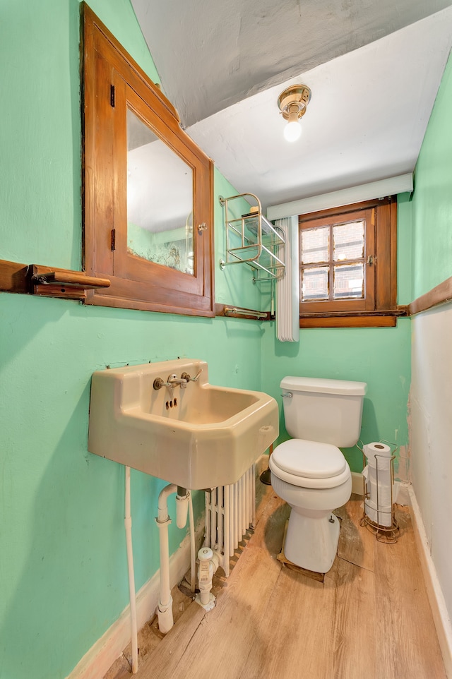 half bath with toilet, baseboards, and wood finished floors