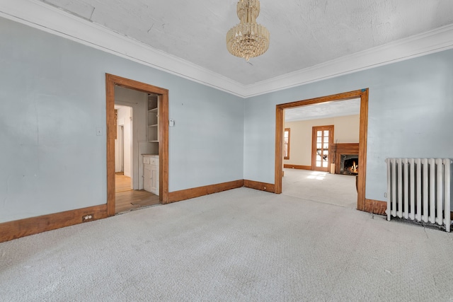 spare room featuring a warm lit fireplace, baseboards, light colored carpet, radiator heating unit, and ornamental molding