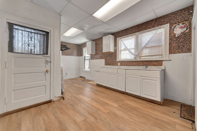 kitchen with white cabinets, a wainscoted wall, light wood-style flooring, light countertops, and a paneled ceiling