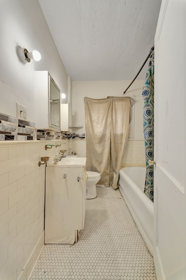 full bathroom featuring shower / bath combo, toilet, a textured ceiling, vanity, and tile walls