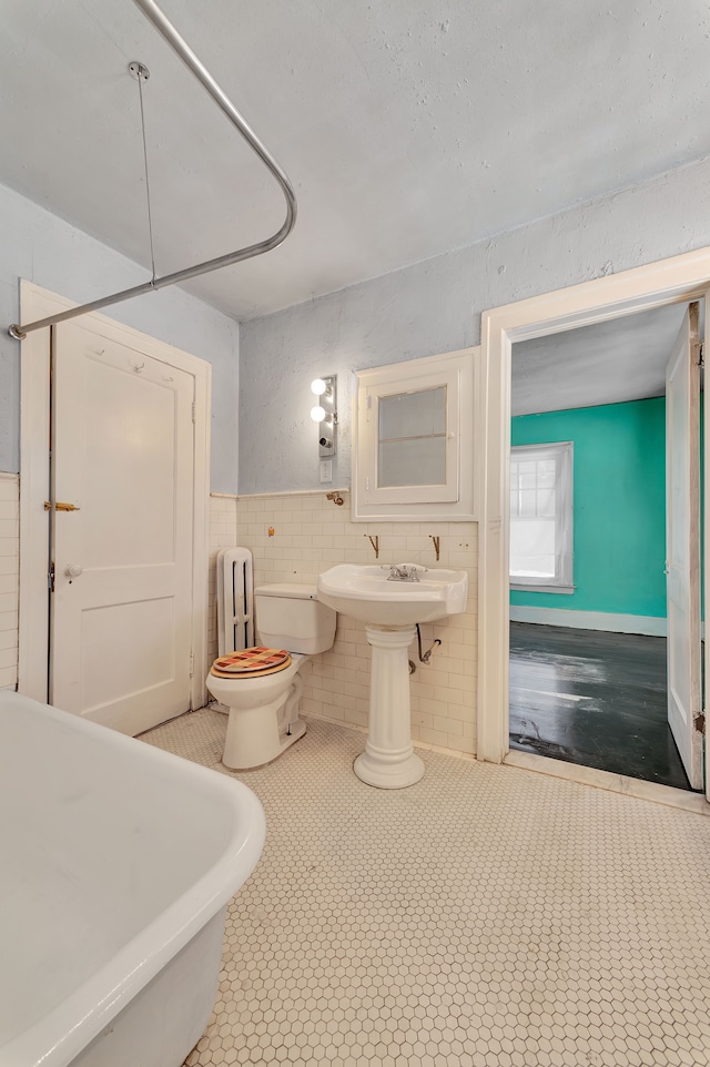 full bath with toilet, tile walls, a soaking tub, tile patterned floors, and radiator