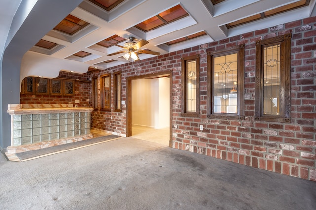 unfurnished living room with coffered ceiling, light carpet, brick wall, and a ceiling fan