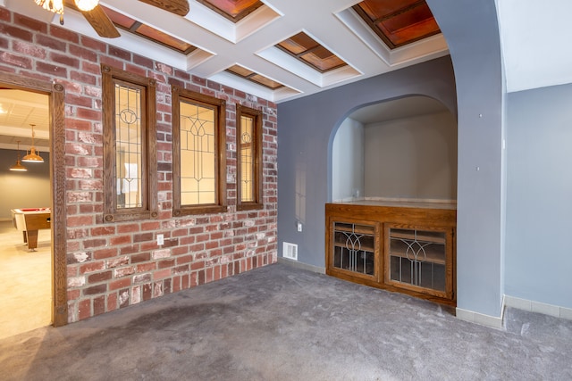 unfurnished living room with visible vents, coffered ceiling, brick wall, dark colored carpet, and beam ceiling