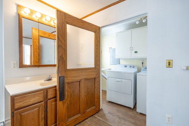 laundry area featuring a sink, light wood-type flooring, cabinet space, electric panel, and washing machine and clothes dryer