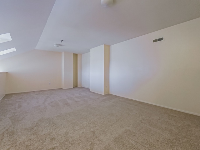 spare room with vaulted ceiling with skylight, visible vents, and light colored carpet