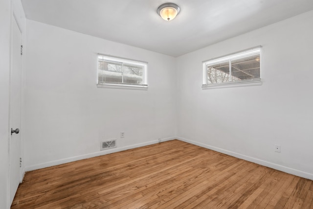 empty room with wood finished floors, visible vents, and baseboards