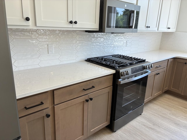 1973 Lowe Dr, Spring Lake, MI 49456 - kitchen featuring gas range, stainless steel microwave, tasteful backsplash, light wood finished floors, and light stone countertops