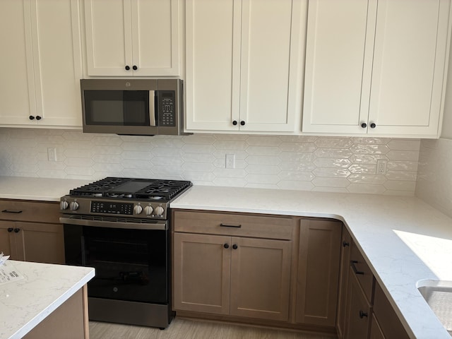 1973 Lowe Dr, Spring Lake, MI 49456 - kitchen with appliances with stainless steel finishes, light stone countertops, decorative backsplash, and white cabinets