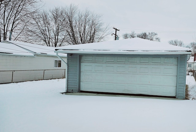 snow covered garage featuring a garage and fence