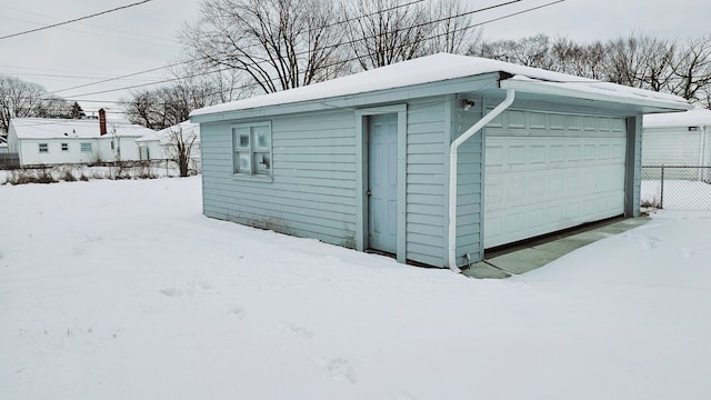 snow covered structure featuring fence and an outbuilding