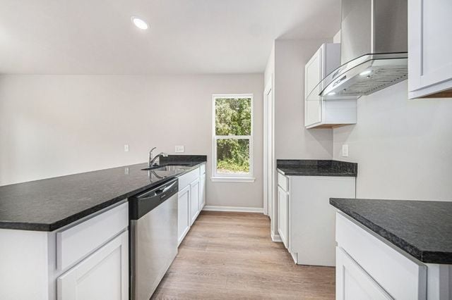 kitchen with dark countertops, light wood-style flooring, stainless steel dishwasher, white cabinets, and ventilation hood