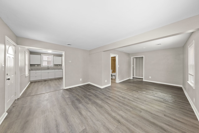 unfurnished living room featuring baseboards, a sink, and light wood-style floors