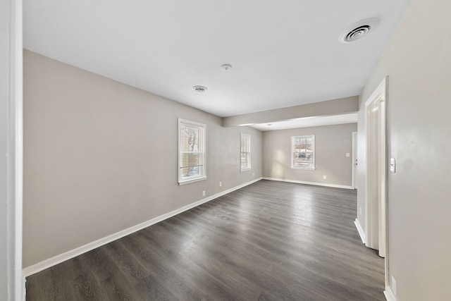 unfurnished room with dark wood finished floors, visible vents, and baseboards