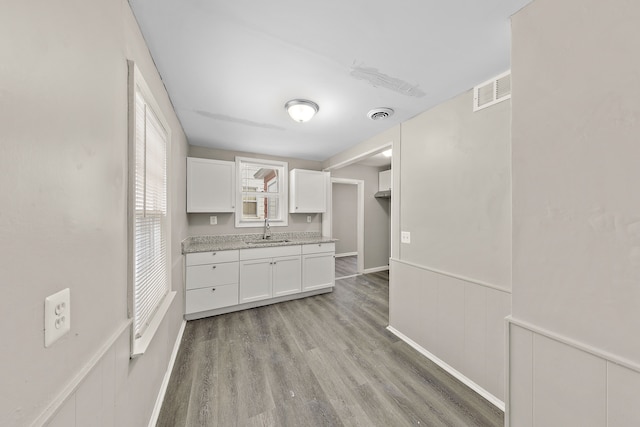 kitchen featuring wainscoting, light countertops, light wood-type flooring, white cabinetry, and a sink