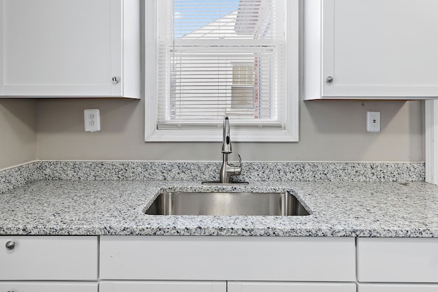 kitchen featuring white cabinetry, a sink, and light stone countertops