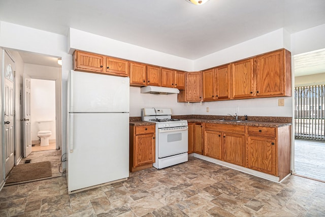 kitchen featuring white appliances, dark countertops, brown cabinets, under cabinet range hood, and a sink