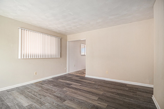 unfurnished room featuring dark wood-style floors, visible vents, a textured ceiling, and baseboards