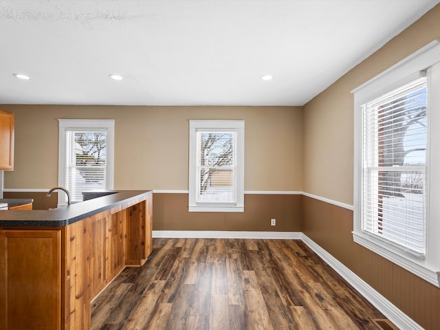 kitchen featuring dark wood-style flooring, a sink, wainscoting, brown cabinetry, and dark countertops