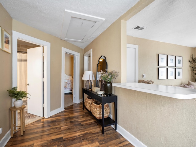 hallway with baseboards, a textured ceiling, visible vents, and dark wood-style flooring