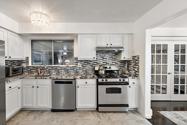 kitchen featuring stainless steel appliances, white cabinetry, a sink, dark stone counters, and under cabinet range hood