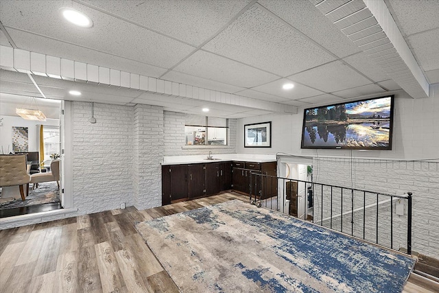 bar with brick wall, light wood finished floors, a sink, and a paneled ceiling