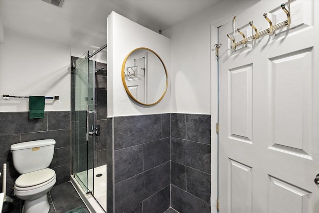 bathroom with wainscoting, toilet, tile patterned floors, a shower stall, and tile walls