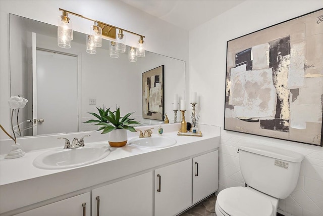 bathroom with double vanity, tile walls, toilet, and a sink