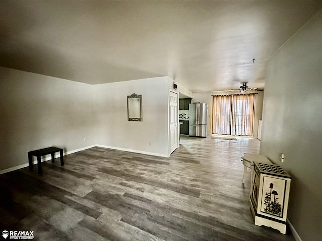 unfurnished living room with dark wood-type flooring, a ceiling fan, and baseboards