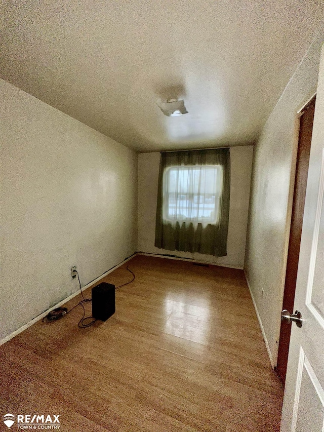 spare room with a textured ceiling, baseboards, and wood finished floors