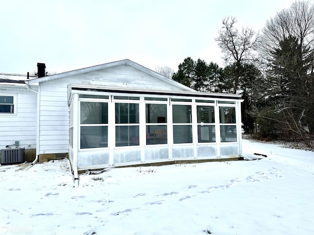 snow covered property featuring a garage, a sunroom, and central AC unit