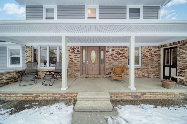 snow covered property entrance with a porch and brick siding