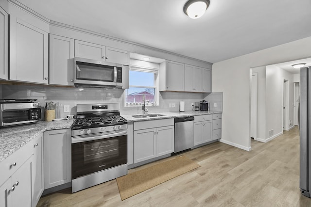 kitchen featuring light stone counters, light wood-style flooring, a sink, appliances with stainless steel finishes, and tasteful backsplash