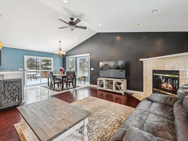 living area featuring lofted ceiling, ceiling fan with notable chandelier, wood finished floors, baseboards, and a tiled fireplace