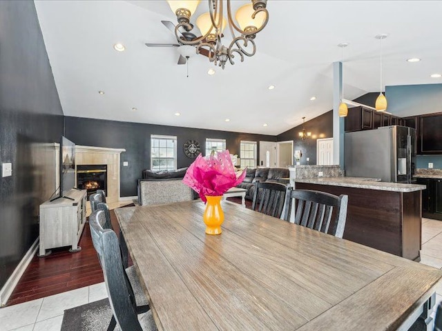 dining room with light tile patterned floors, baseboards, a premium fireplace, vaulted ceiling, and a notable chandelier