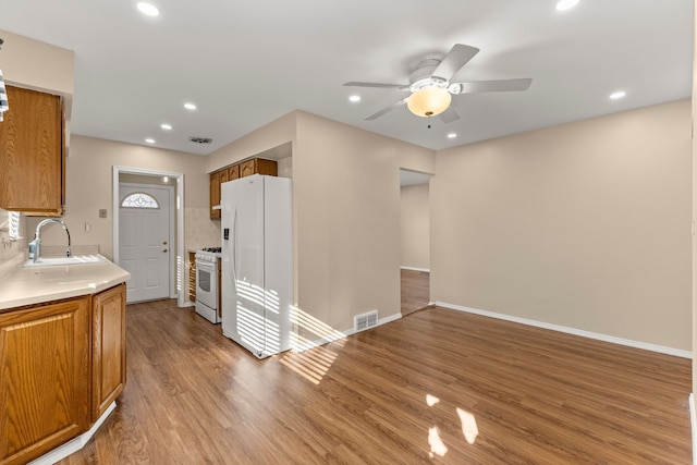 kitchen featuring brown cabinets, light countertops, a sink, wood finished floors, and white appliances