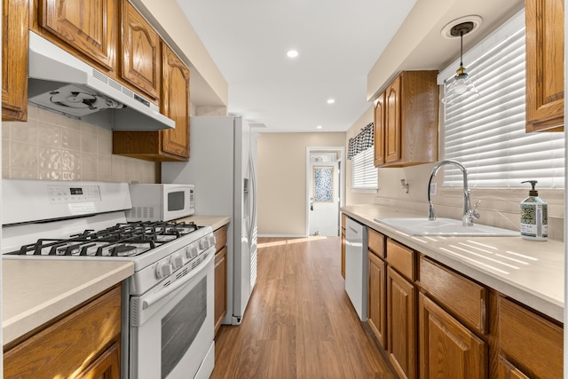 kitchen with white appliances, decorative light fixtures, light countertops, under cabinet range hood, and a sink