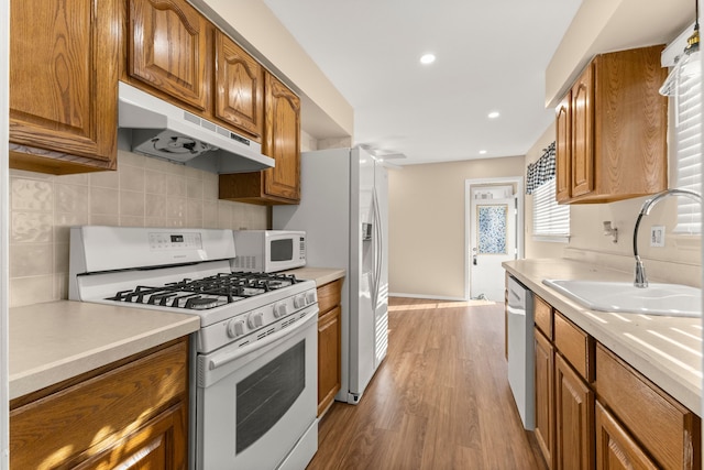 kitchen with under cabinet range hood, white appliances, a sink, light countertops, and brown cabinetry