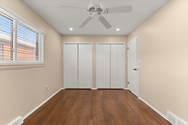 unfurnished bedroom with dark wood-style floors, baseboards, visible vents, and multiple closets