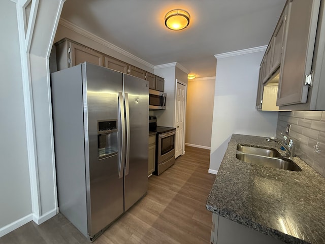 kitchen featuring light wood finished floors, stainless steel appliances, backsplash, ornamental molding, and a sink