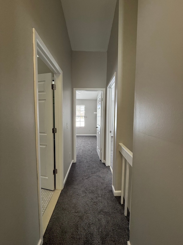 hall with baseboards and dark colored carpet