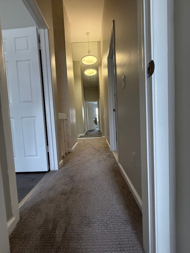 hallway featuring dark colored carpet and baseboards