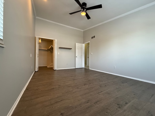 unfurnished bedroom with visible vents, baseboards, dark wood-style floors, ornamental molding, and a walk in closet