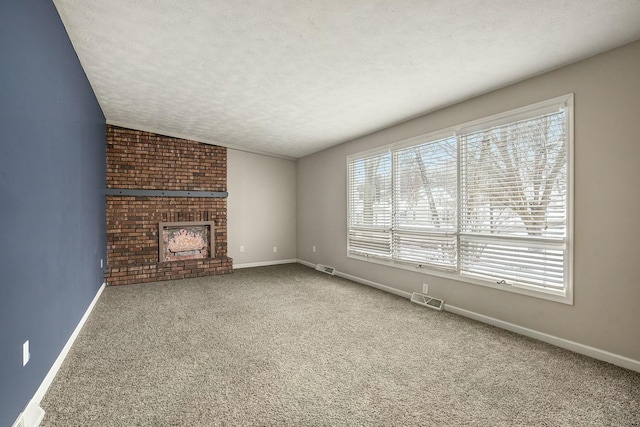 unfurnished living room with a textured ceiling, visible vents, baseboards, a brick fireplace, and carpet