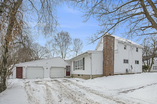 snow covered property featuring a chimney and an attached garage