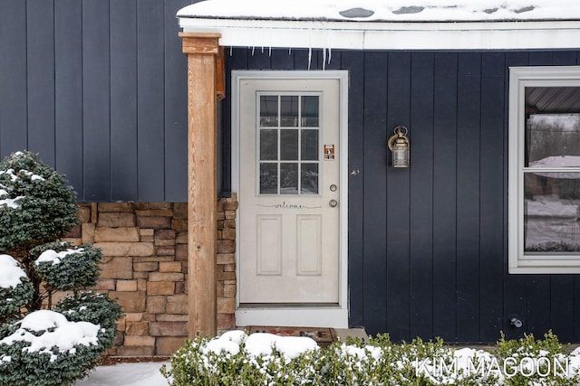 snow covered property entrance featuring stone siding