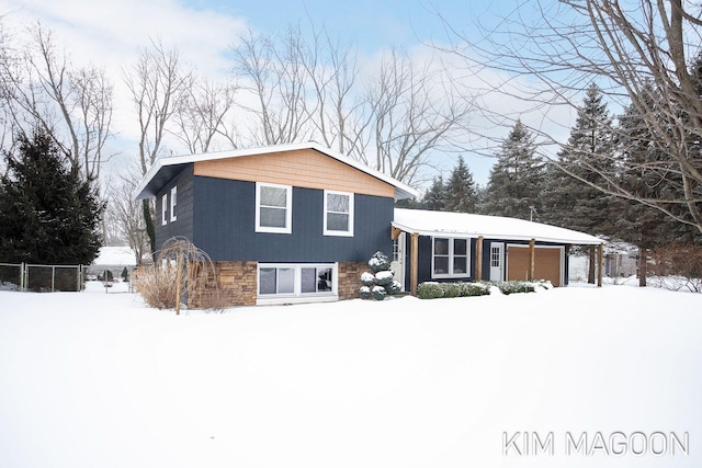 tri-level home featuring a garage, stone siding, and fence