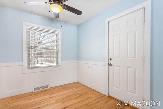 empty room featuring a wainscoted wall, visible vents, ceiling fan, and light wood-style flooring