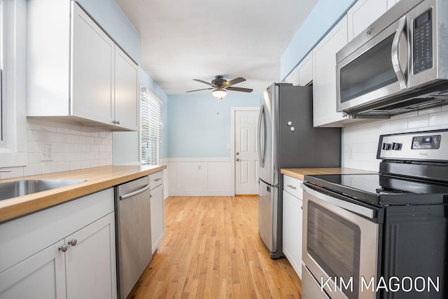 kitchen featuring white cabinets, stainless steel appliances, wooden counters, and wainscoting