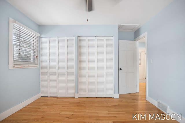 unfurnished bedroom featuring visible vents, baseboards, multiple closets, light wood-type flooring, and attic access