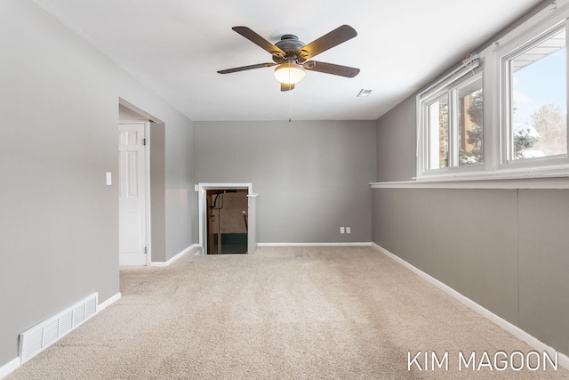 empty room featuring a ceiling fan, visible vents, light carpet, and baseboards